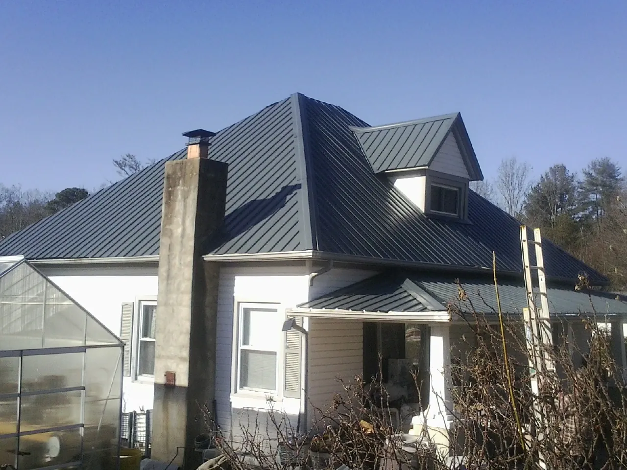 Dark blue standing seam metal roof on a white farmhouse with dormer — Slate & Tile Roof Repair by Roofing Brothers in Plano
