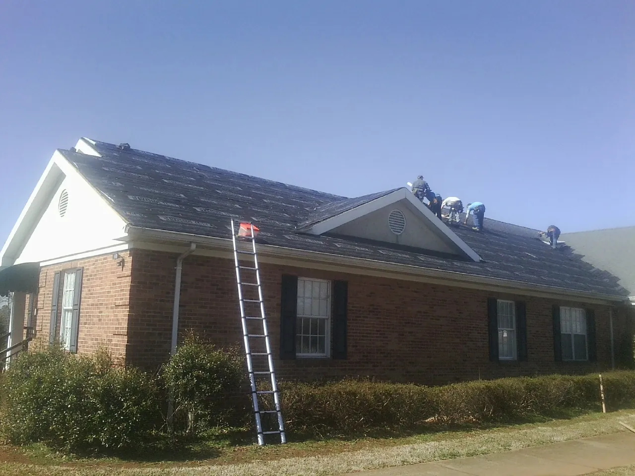 Crew tearing shingles off a brick ranch roof with a ladder set — Emergency Roof Repair work by our crew in Plano