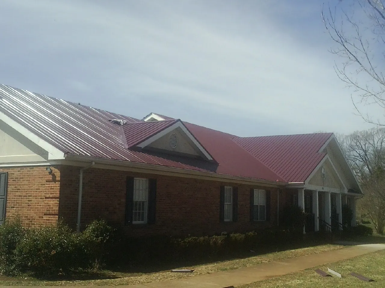 Red metal roof with gabled entries on a long brick building, from a Hail Damage Roof Repair job in Plano